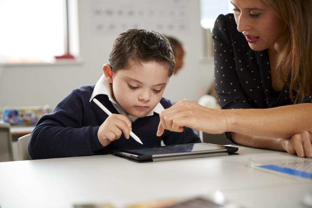 在一所小学的教室里，年轻的女老师正在和一个患有唐氏综合症的男孩一起使用平板电脑, 前视图, 近距离